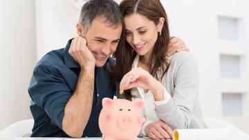 Portrait Of Happy Couple Inserting Coin In Piggybank